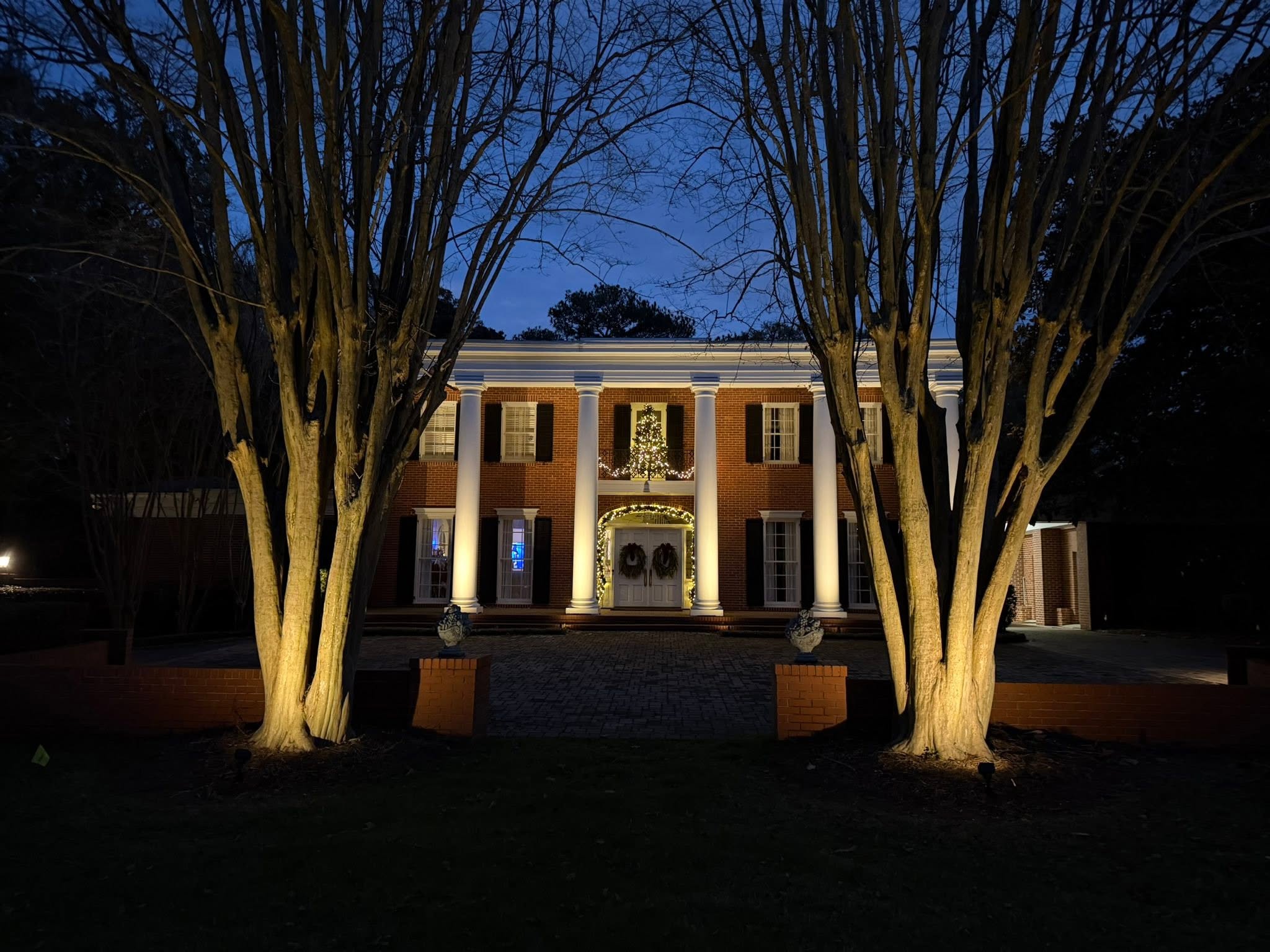 Columned estate with crepe myrtles uplit in gold at dusk