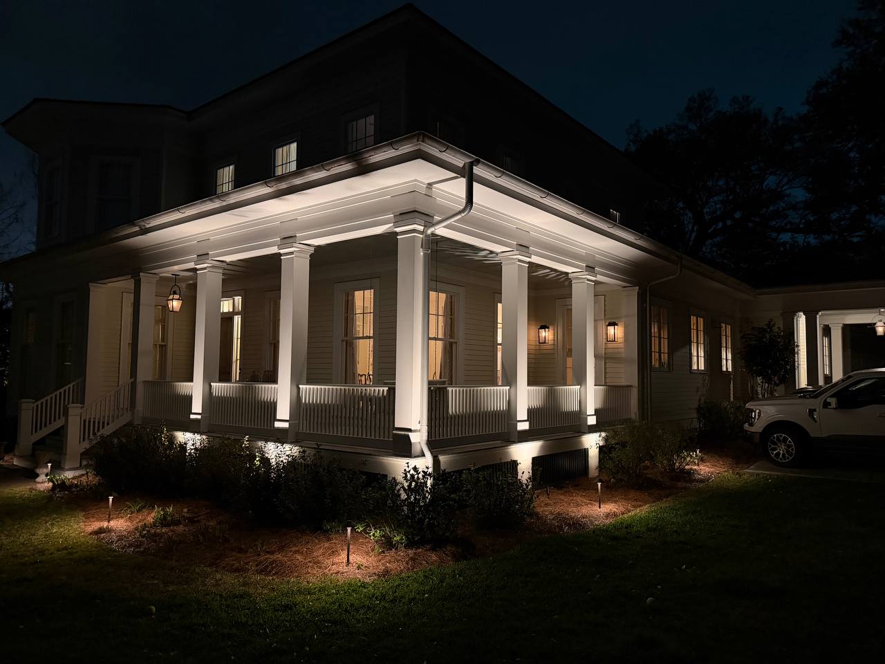 White-columned front porch and garden path glowing at dusk with warm architectural lighting