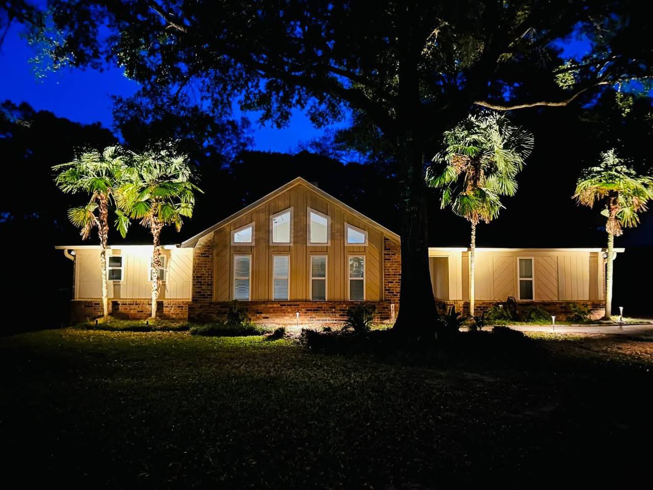 Single-story home with palms and warm facade lighting at blue hour