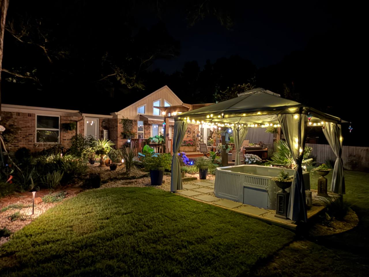 Wide nighttime view of a home and spa garden with layered warm landscape lighting